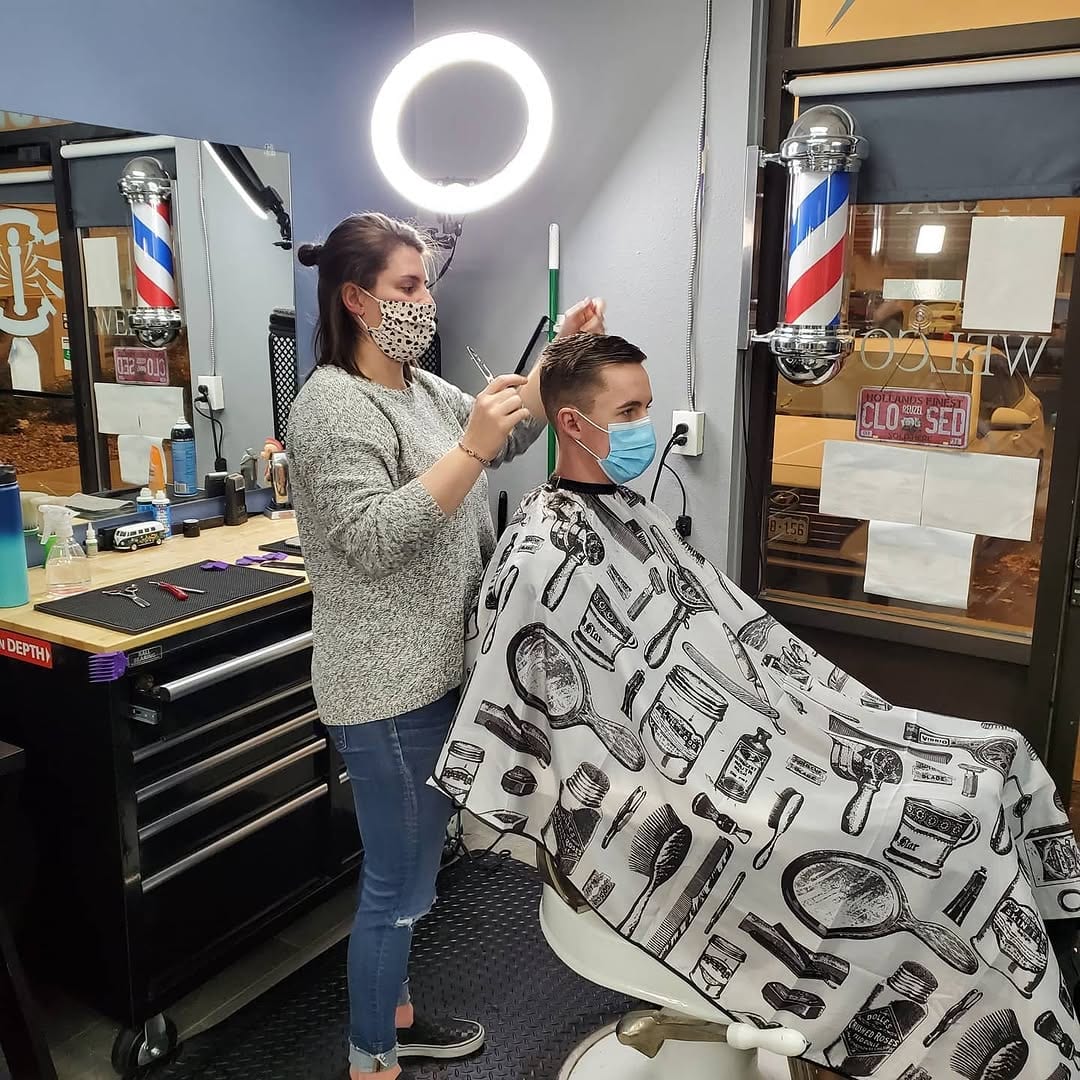 A barber trimming a client's hair beneath a circular light