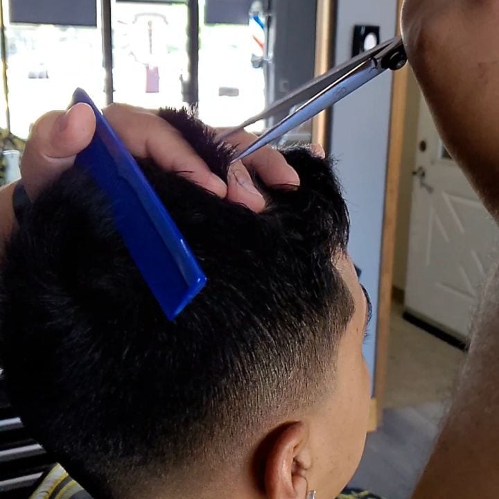 Scissors and a blue comb working through dark hair