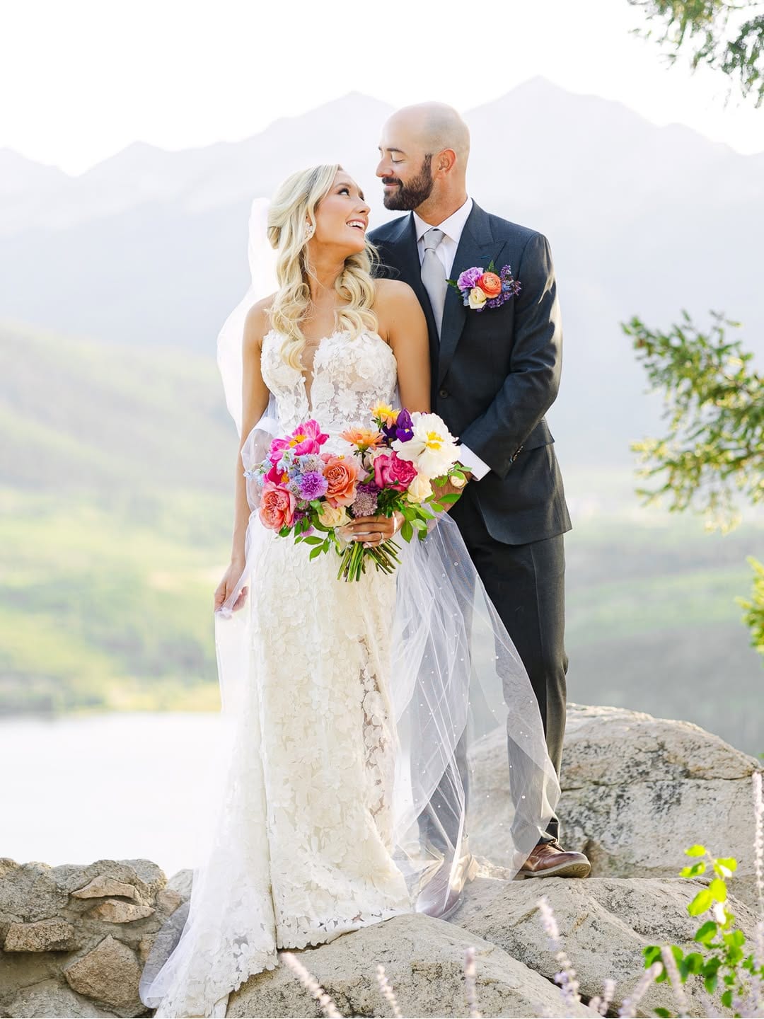Bride and groom embracing on rocks with Colorado mountains behind them
