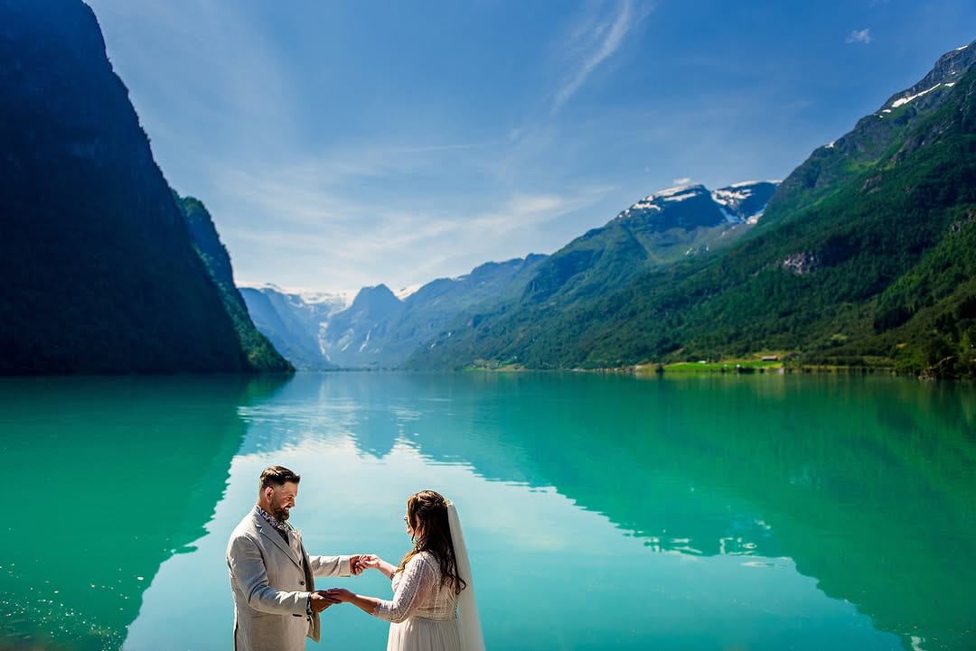 A couple beside a turquoise fjord and steep green mountains