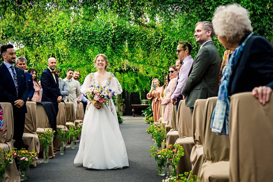A smiling bride walking down an outdoor wedding aisle