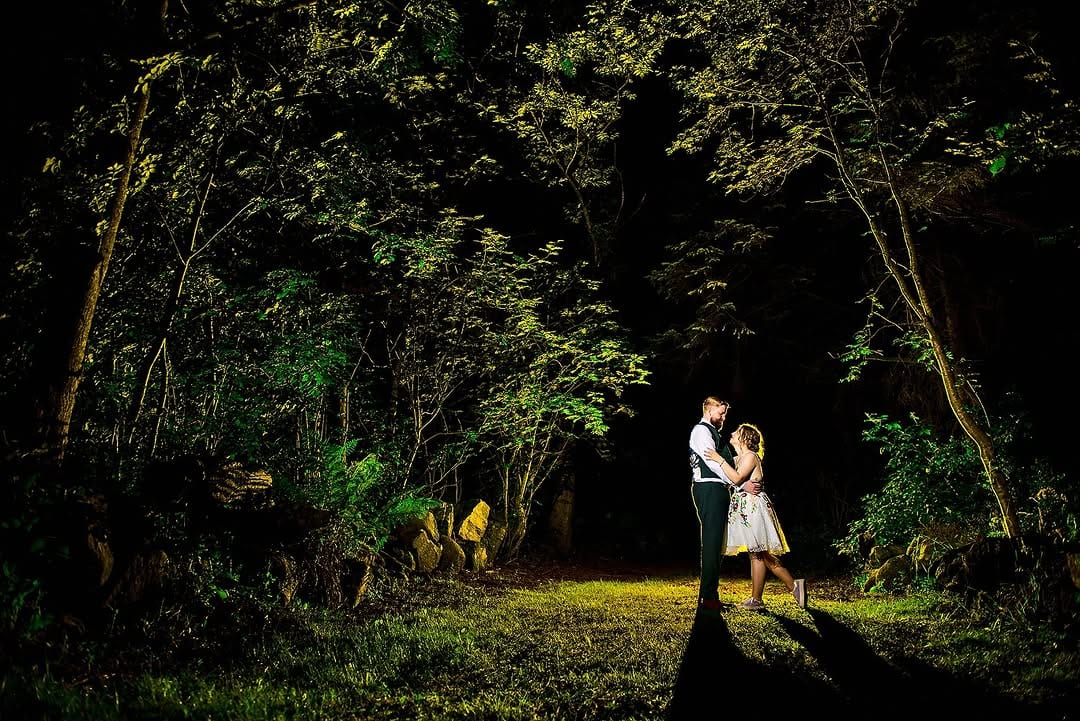 A couple standing together in a dark forest clearing
