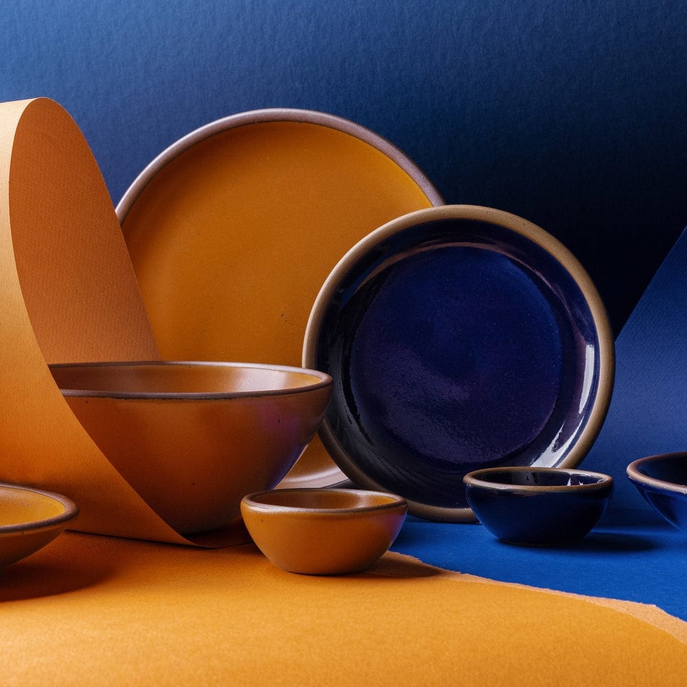 Orange and dark blue ceramic plates and bowls arranged in a bold studio composition.