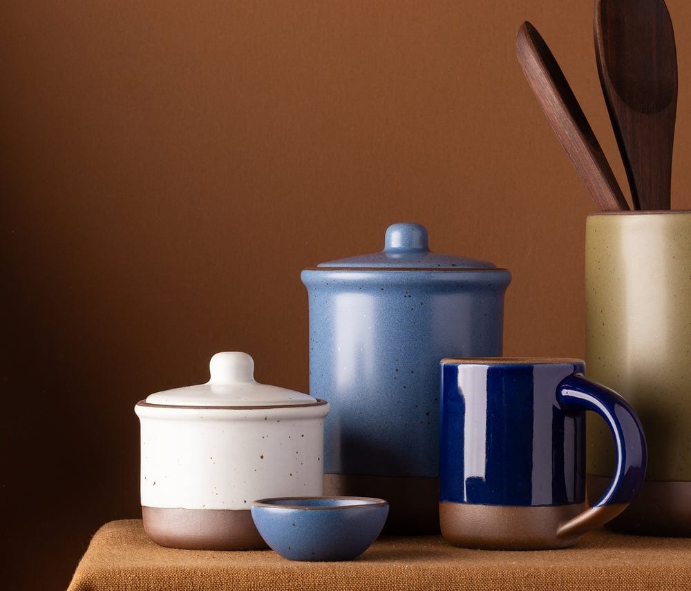 Ceramic jars, utensil crock, mug and bowl arranged on a shelf.