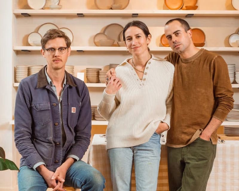 Three people standing in front of shelves filled with ceramic plates and dishes.