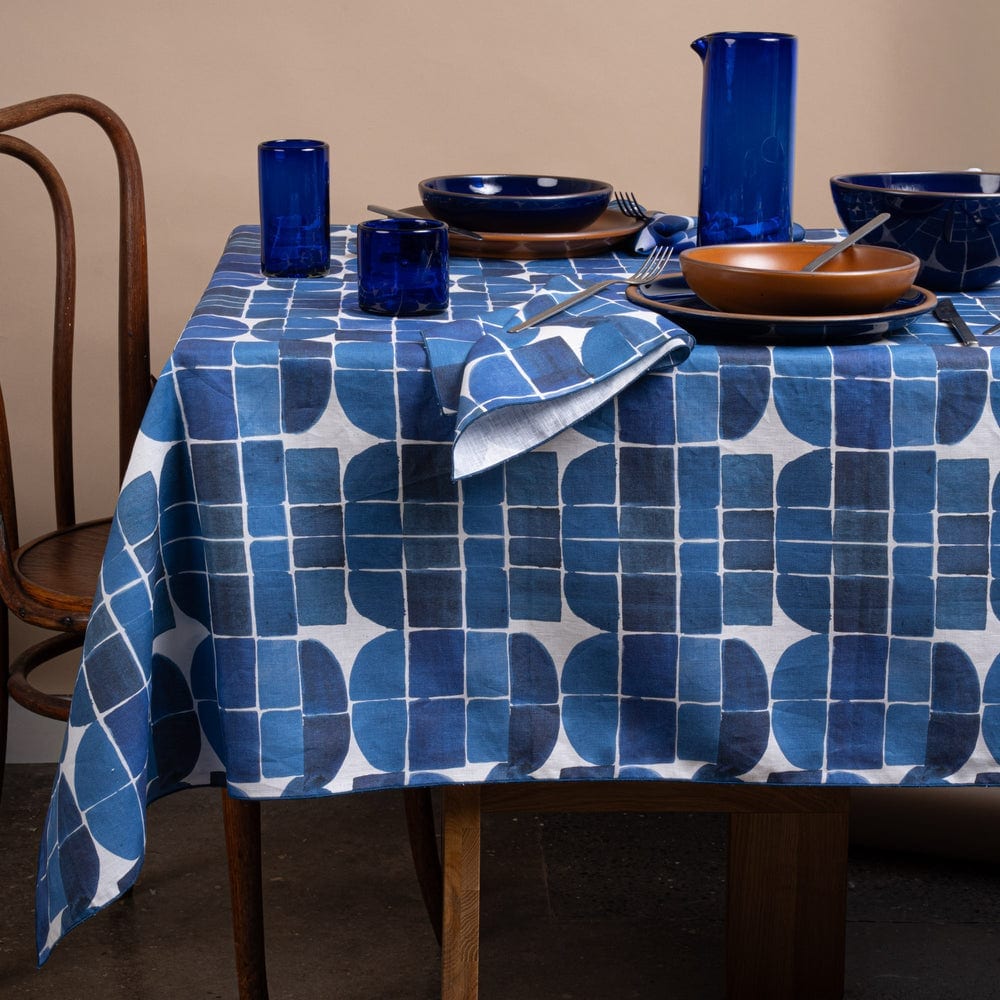 Dinner table set with blue glassware, ceramic plates and a patterned cloth.