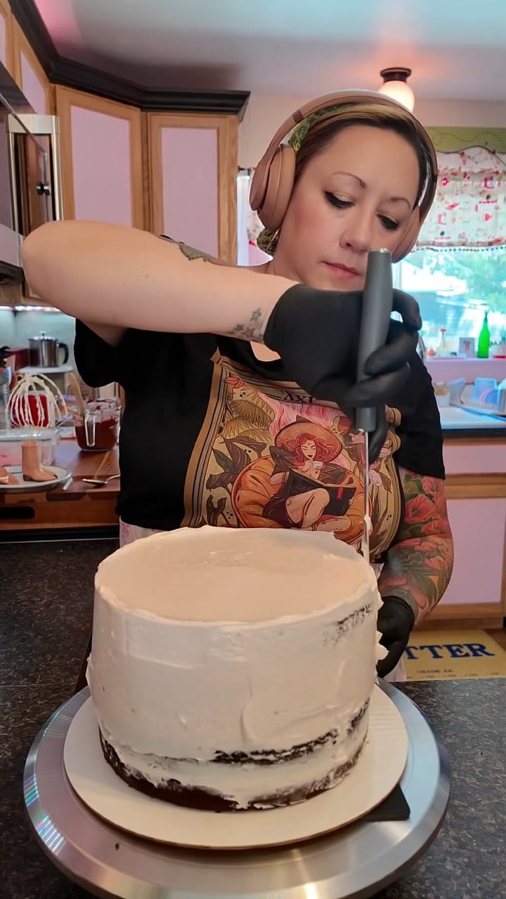 Tattooed baker smoothing frosting onto a round cake