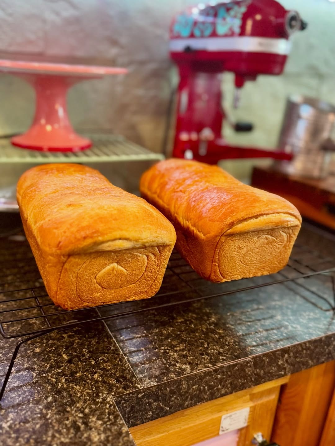 Golden loaves cooling on a wire rack beside a red stand mixer
