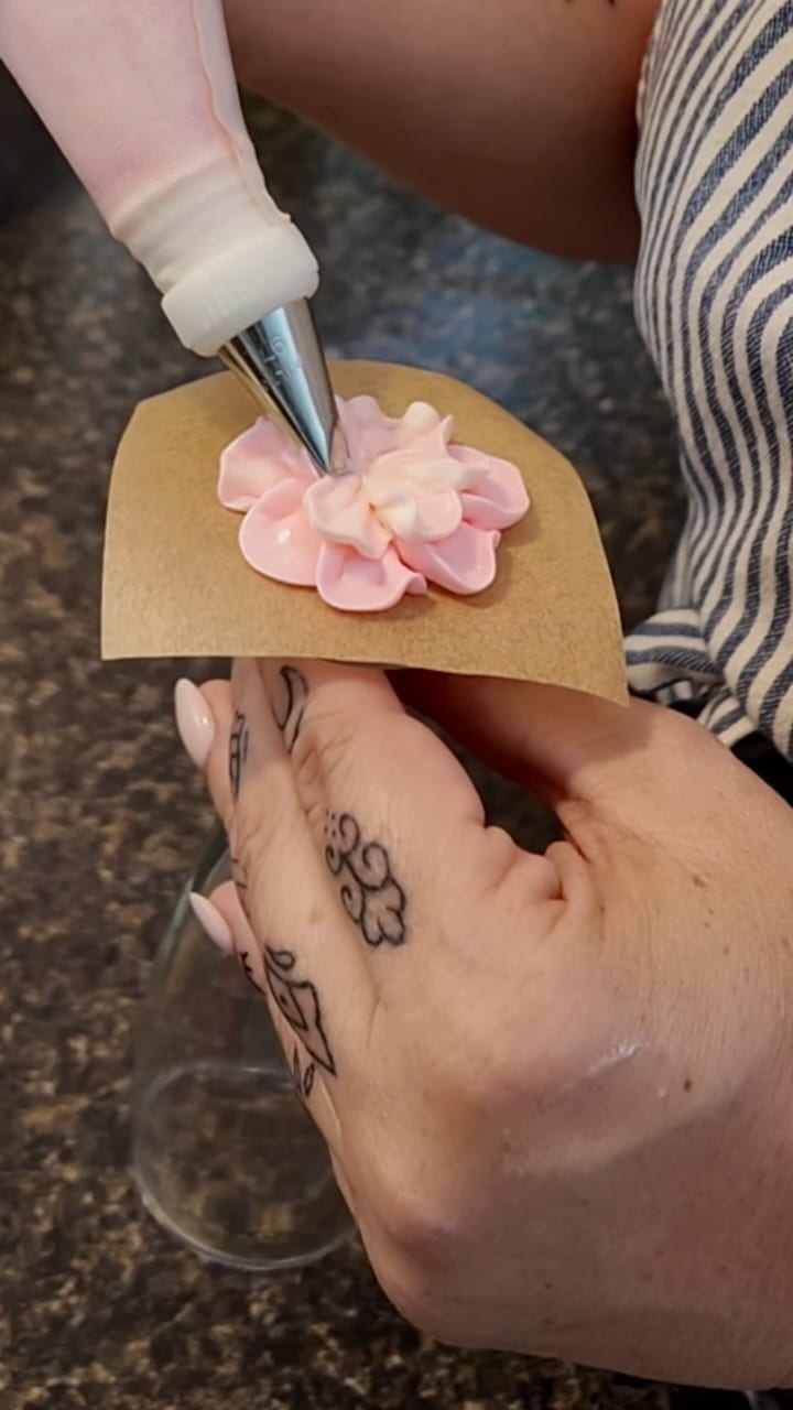 Gloved hands piping pink buttercream flowers over a wine glass