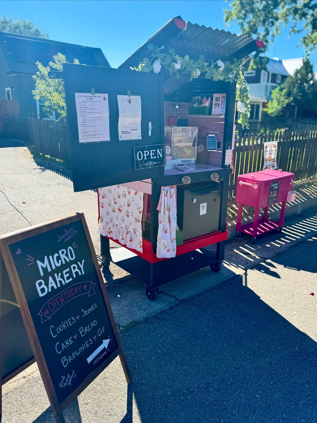 Small dark outdoor bakery cart with an OPEN sign and chalkboard menu