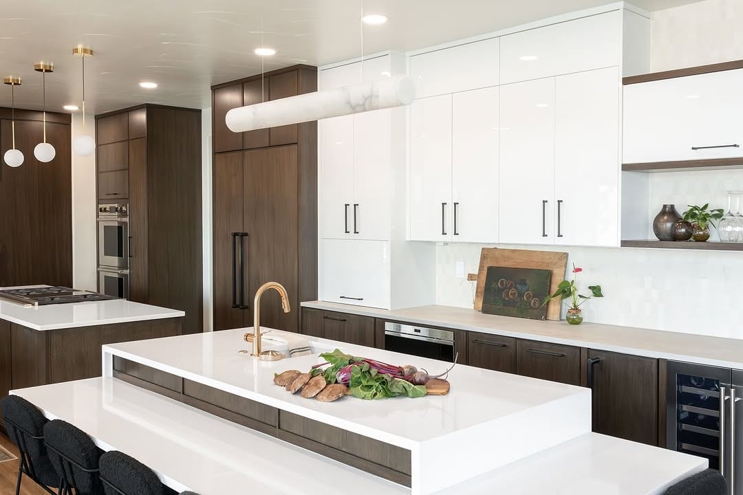 Bright modern kitchen with white cabinetry, dark wood cabinets, a large island and pendant lights.
