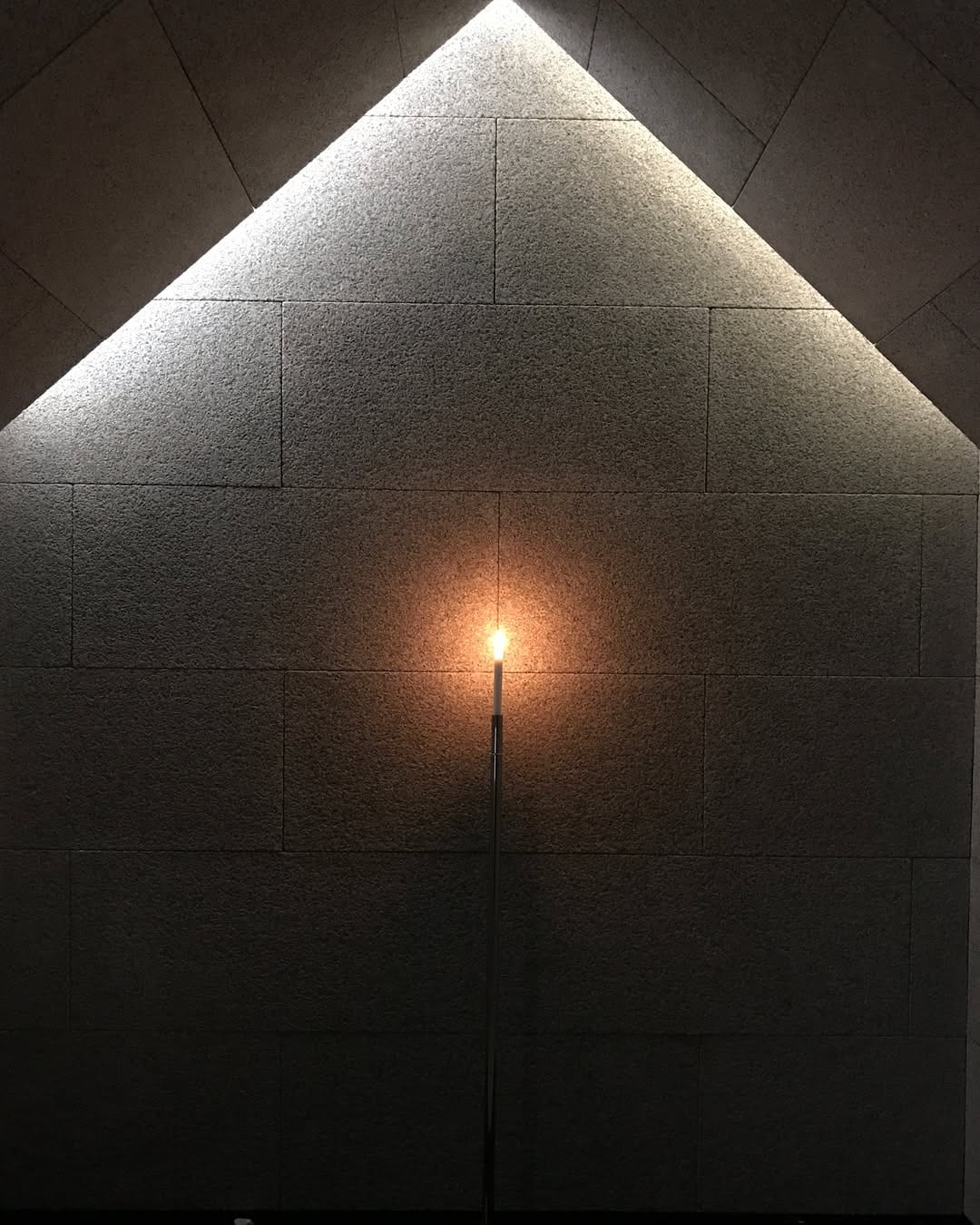 Dark architectural interior with a triangular beam of light on a textured wall.