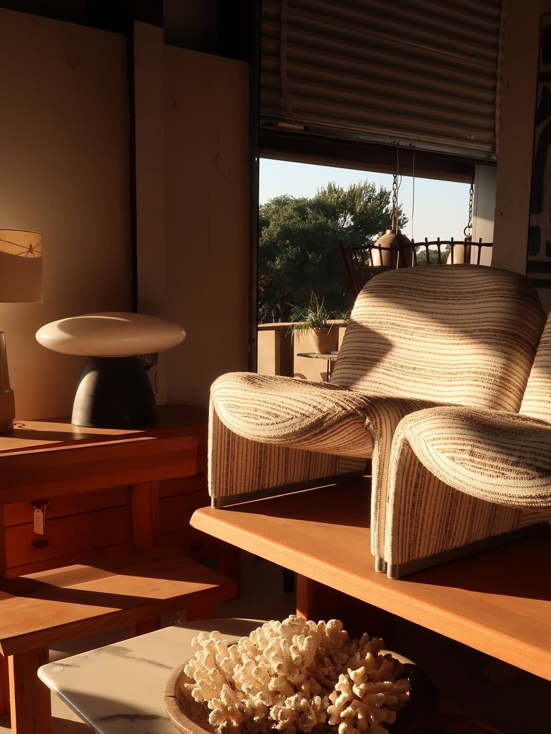 Warmly lit room with a woven lounge chair, wood furniture and a small table lamp.