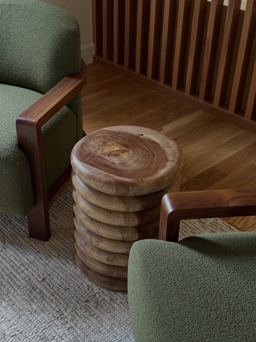Two green upholstered wooden chairs and round wooden stools on a textured rug.