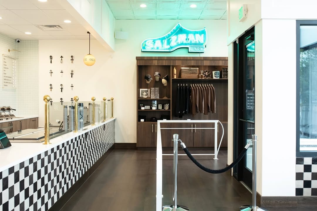 Bright commercial interior with a checkerboard counter, display cases, dark wood shelving and a turquoise sign.