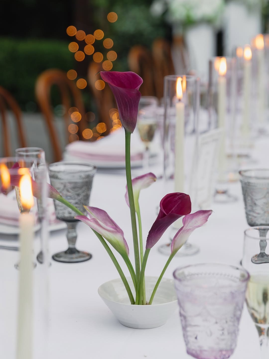 Wedding reception table with candles, glassware, and purple calla lilies