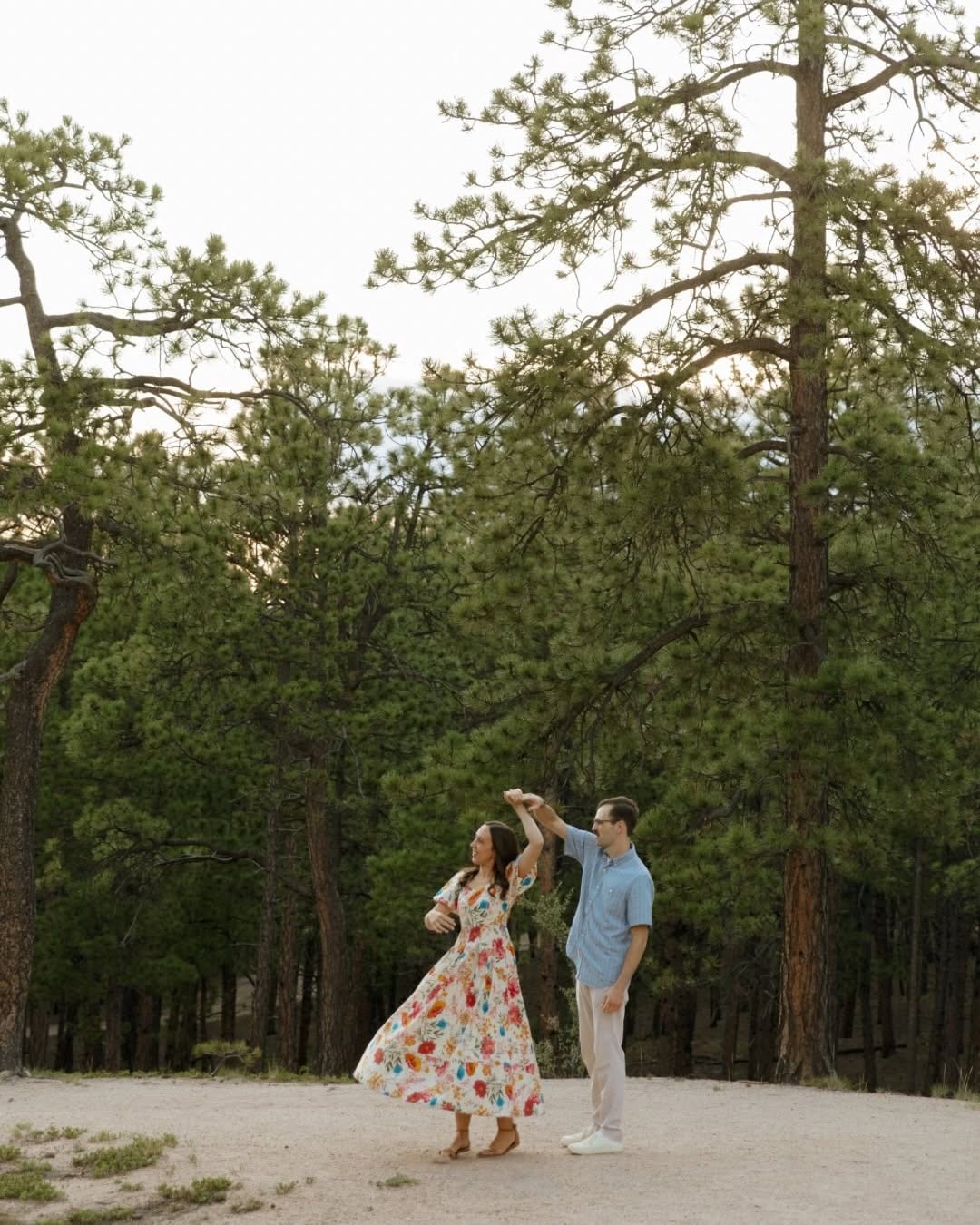 Couple walking and dancing on a dirt path among tall pine trees