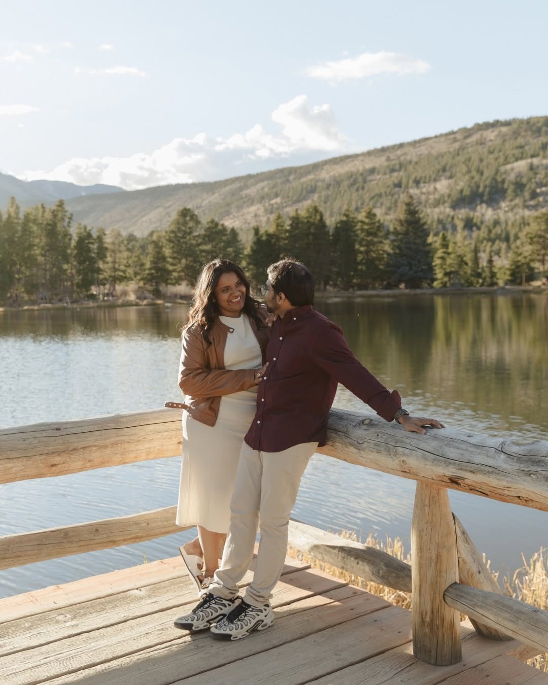 Couple standing together on a wooden dock beside a mountain lake