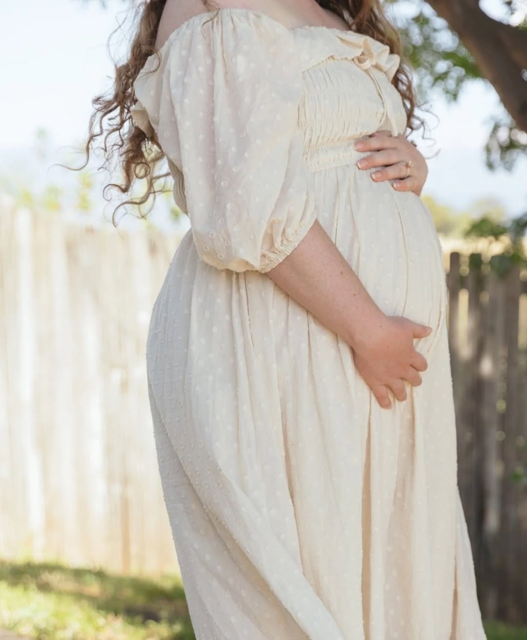 Pregnant person holding their belly with another hand resting on their abdomen