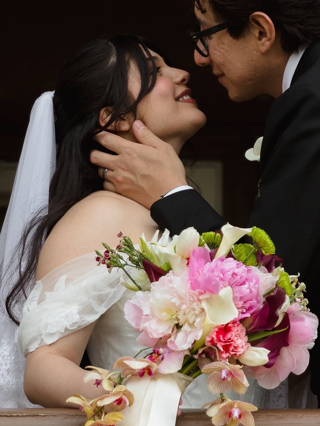 Bride and groom embracing closely while holding a colorful bouquet