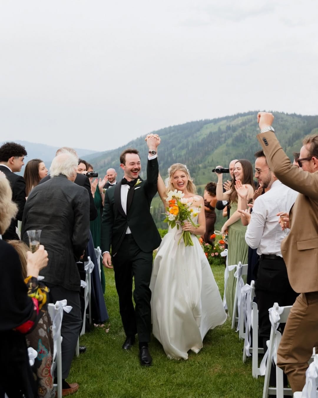 Bride and groom walking between cheering wedding guests with mountains behind them